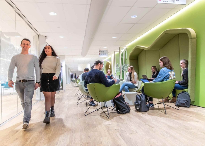Studenten lopen in een gang langs andere studenten die op hun laptop aan het werk zijn