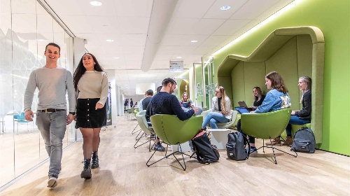 Studenten lopen in een gang langs andere studenten die op hun laptop aan het werk zijn